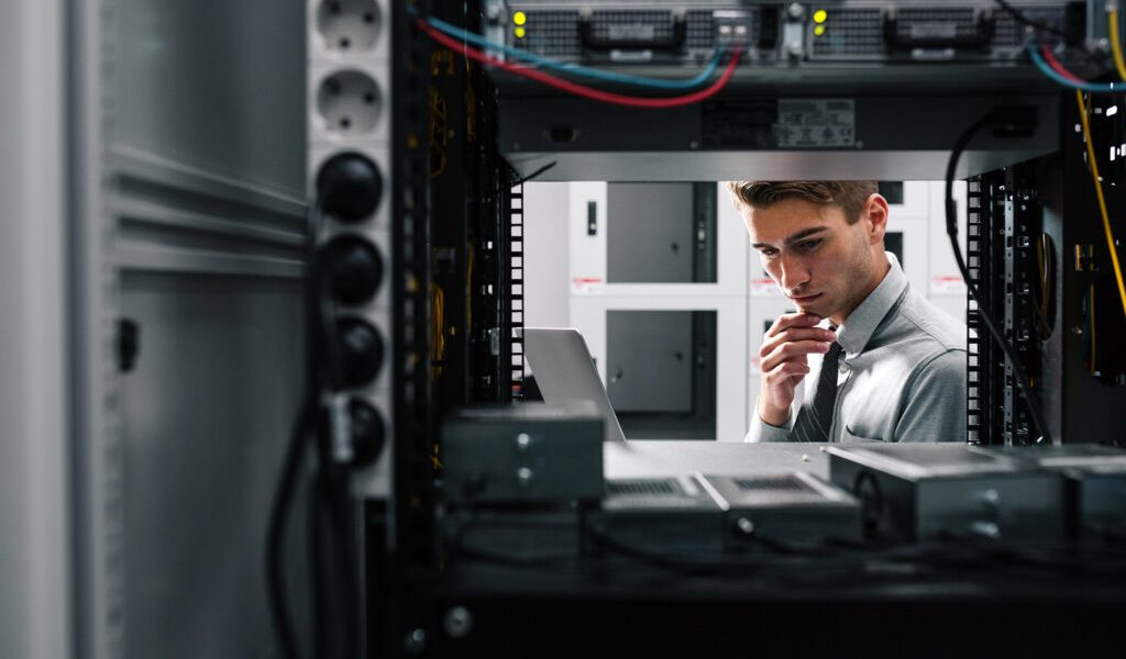 IT-Fachmann inspiziert ein Server-Rack und betrachtet einen Laptop in einem Rechenzentrum.