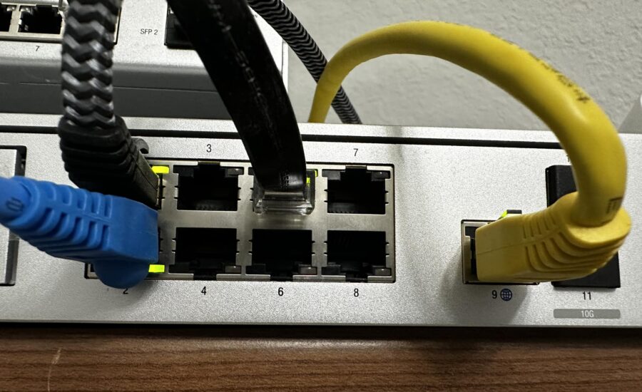 Netzwerk-Switch mit blauem und gelbem Ethernet-Kabel, die in Ports eingesteckt sind, zeigt Portnummern und verwendete Kabel.