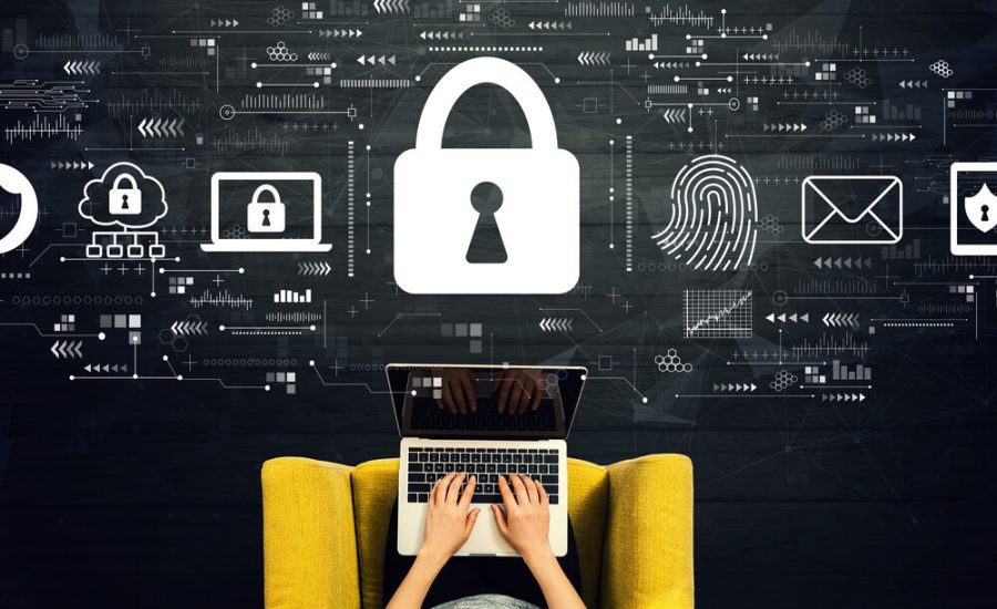 Person tippt auf einen Laptop auf einem gelben Stuhl, mit einem großen Vorhängeschloss und digitalen Sicherheitssymbolen, die darüber schweben, was Cybersicherheit veranschaulicht.