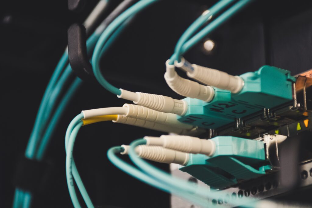 A close-up of teal Ethernet cables plugged into a network patch panel in a server rack, in dim lighting.