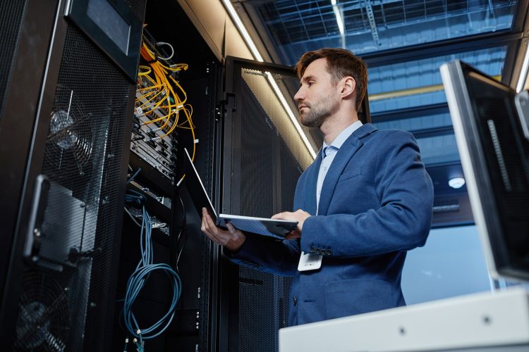 IT-Fachmann im blauen Anzug inspiziert Server-Racks mit einem Laptop in einem Rechenzentrum