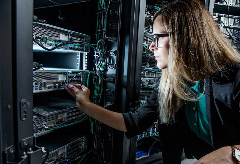 A female IT technician in a data centre plugs a network cable into a rack-mounted server.