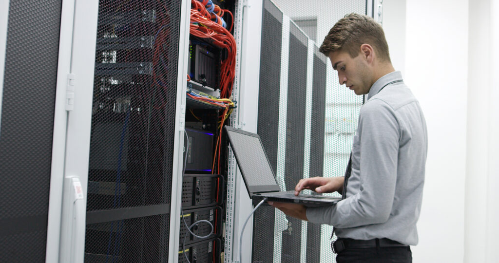 Técnico informático que utiliza un ordenador portátil para configurar servidores en la sala de cableado de un centro de datos