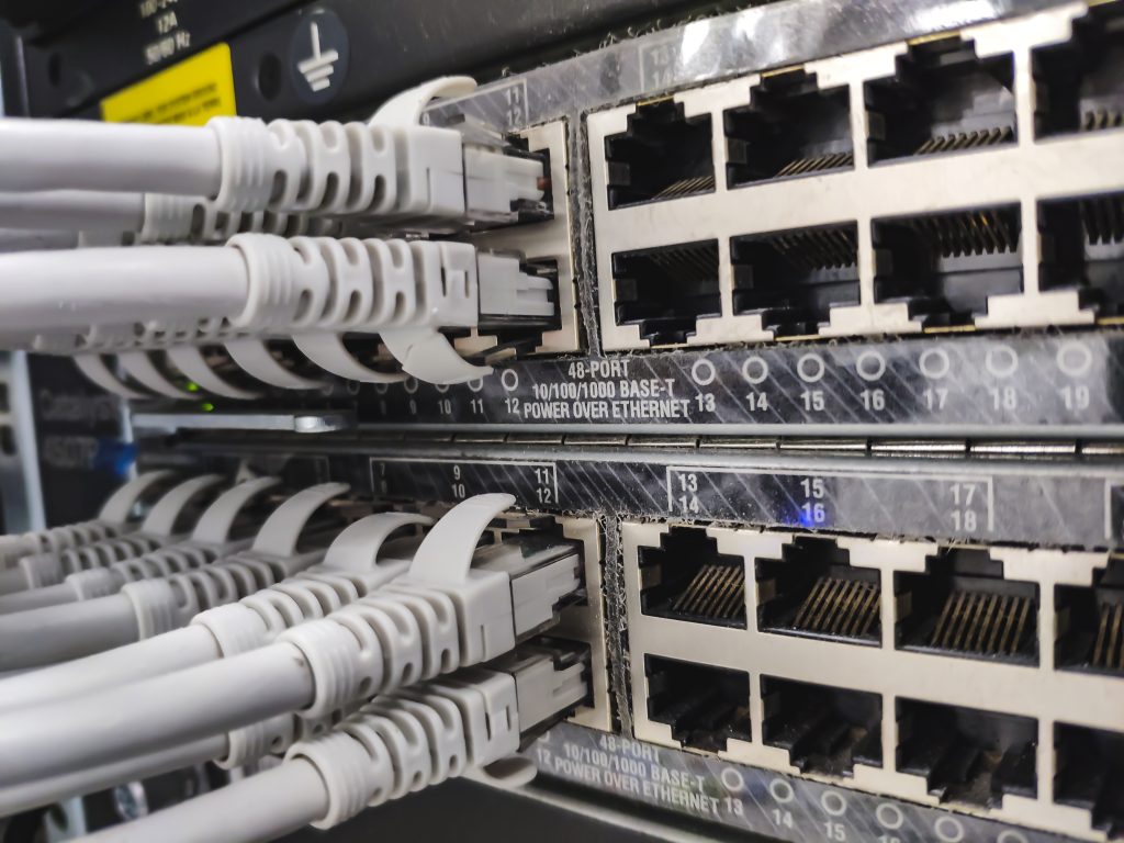 A close-up of a network patch panel with multiple RJ-45 Ethernet ports and grey cables plugged into them in a server rack, showing the data cabling.