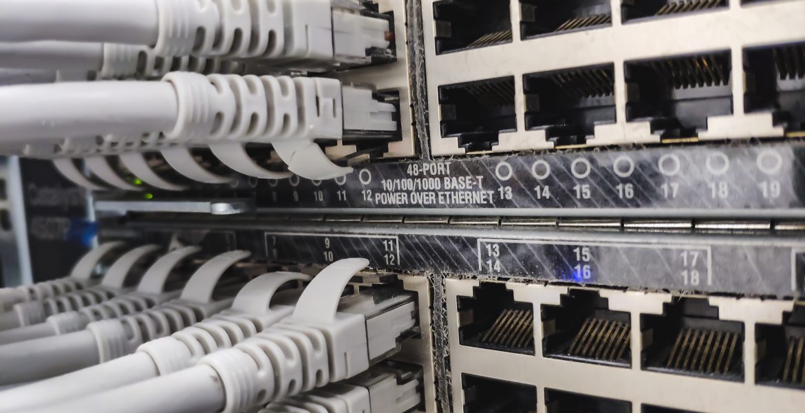 A close-up of a network patch panel with multiple RJ-45 Ethernet ports and grey cables plugged into them in a server rack, showing the data cabling.