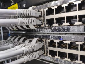 Close-up of a network patch panel with multiple RJ-45 Ethernet ports and gray cables plugged into them in a server rack, showing data cabling.