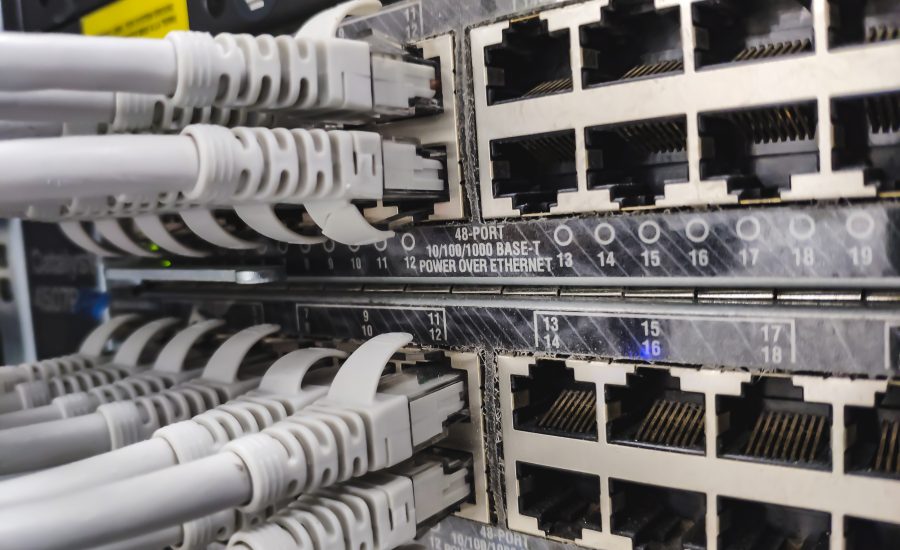 Nahaufnahme eines Netzwerk-Patchpanels mit mehreren RJ-45-Ethernet-Anschlüssen und eingesteckten grauen Kabeln in einem Serverschrank, die die Datenverkabelung zeigen.